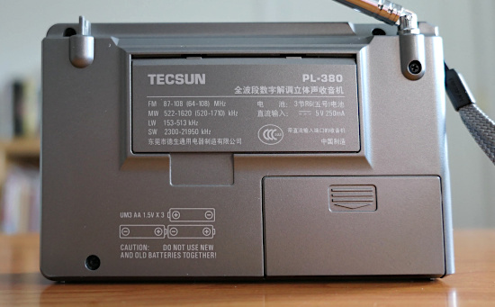 Rear of the Tecsun PL-380 AM/FM/shortwave radio, showing a stand (folded up), the battery compartment, and some text with information about the radio
